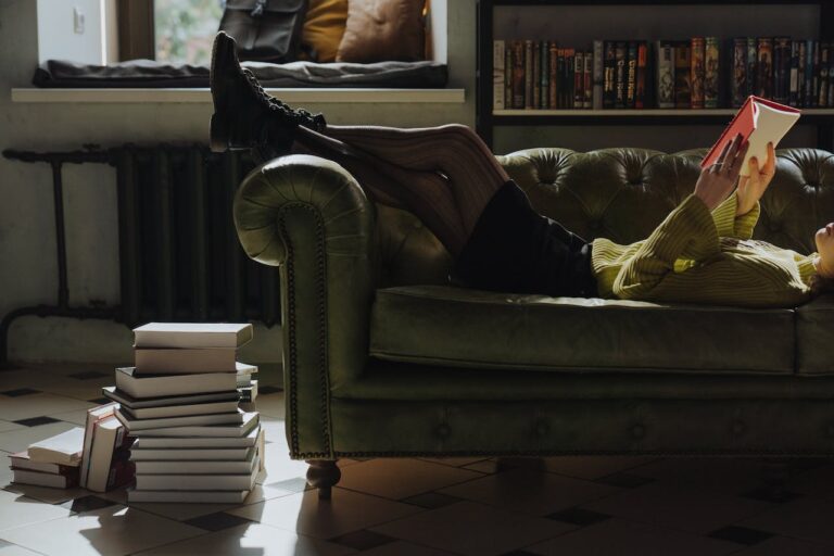 JLNICH blog beats article, Books I’ve Read This Year 2023. Image of woman laying on couch reading with a stack of books on the floor