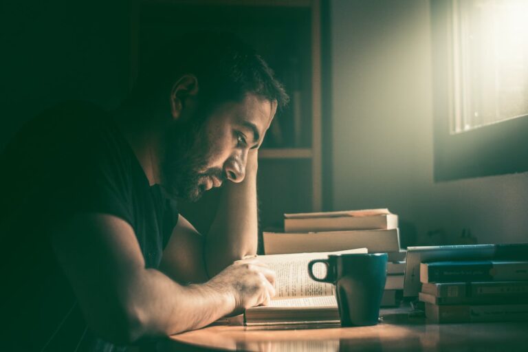 JLNICH blog beats article, Journey to Writerly Excellence: Areas to Strengthen. cover image of man reading books next to a stack of books