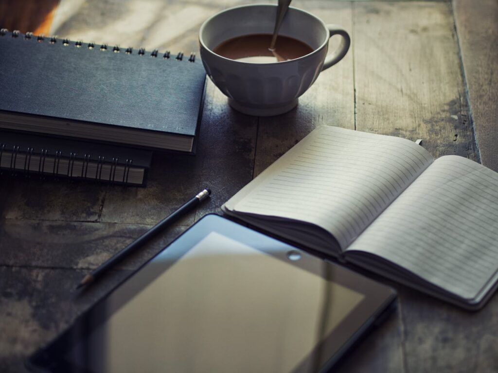 JL NICH blog beats article, Charting the Unknown: SFF Writing Adventures and 2024 Ambitions. Image of book, tablet, tea, and notebook