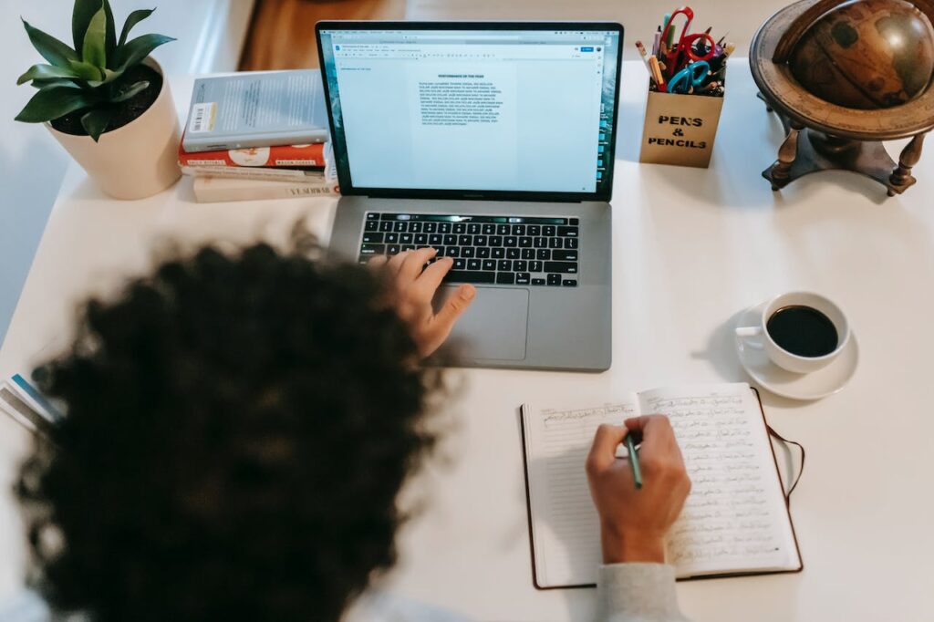 JL NICH blog beats article, SFF Writing Resolutions for the Future: 3-Year and 5-Year. woman typing on a computer and taking notes in a journal.